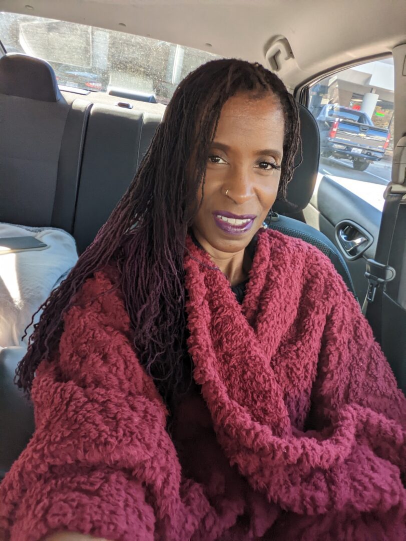A woman sitting in the back of a car wrapped up in a blanket.