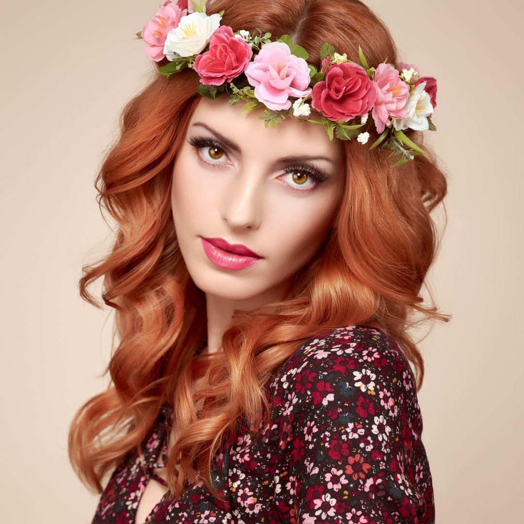 A woman with red hair wearing a floral dress and flower crown.