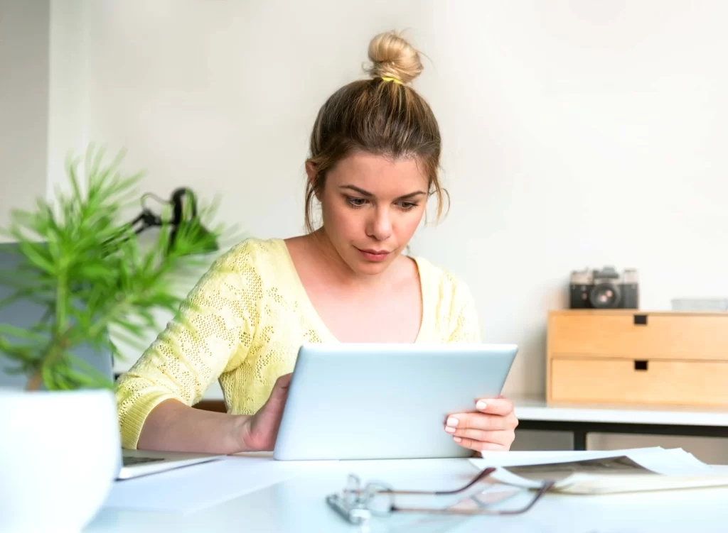 A woman sitting at a table looking at an ipad.